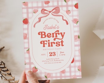 May include: A pink and white gingham patterned invitation with strawberry illustrations. The text reads "Isabel's Berry First Birthday Party" with the date August 23rd and time 3-5PM. A bow and dotted border frame the text.