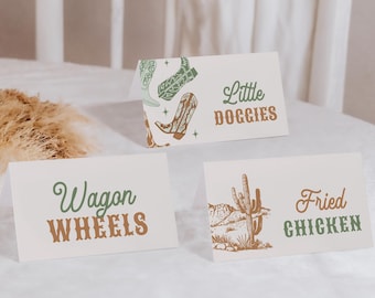 May include: Three white cards with brown and green text and illustrations. The first card says "Wagon Wheels" in brown and green text. The second card says "Little Doggies" in brown text and has a green and brown illustration of cowboy boots. The third card says "Fried Chicken" in brown and green text and has a green and brown illustration of a cactus.