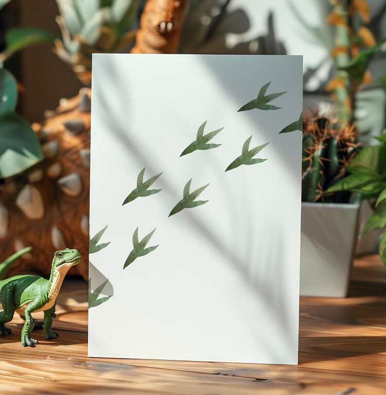 May include: A white card with green dinosaur footprints printed on it. The card is sitting on a wooden table with a green dinosaur toy in the foreground.