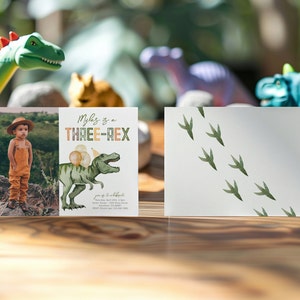May include: A dinosaur-themed birthday invitation with a photo of a child wearing a hat and overalls. The invitation says "Myles is a THREE-REX" and features a green dinosaur with a party hat and balloons. The back of the invitation has a white background with green dinosaur footprints.