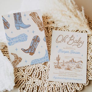 May include: A light blue and brown baby shower invitation with a western theme. The invitation features a desert landscape with cacti and a cowboy boot pattern. The text reads "Oh Baby" and "Join us for a Baby Shower honoring Harper Jensen".