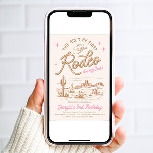 May include: A smartphone displaying a digital invitation with a western theme. The text reads This Ain't My First Rodeo it's my 2nd! Georgia's 2nd Birthday, Saturday, August 22nd, 11am-2pm, Bouncing Off the Walls, 1234 Columbia St. Redmond, WA, RSVP: Kaylee 123-456-7890.