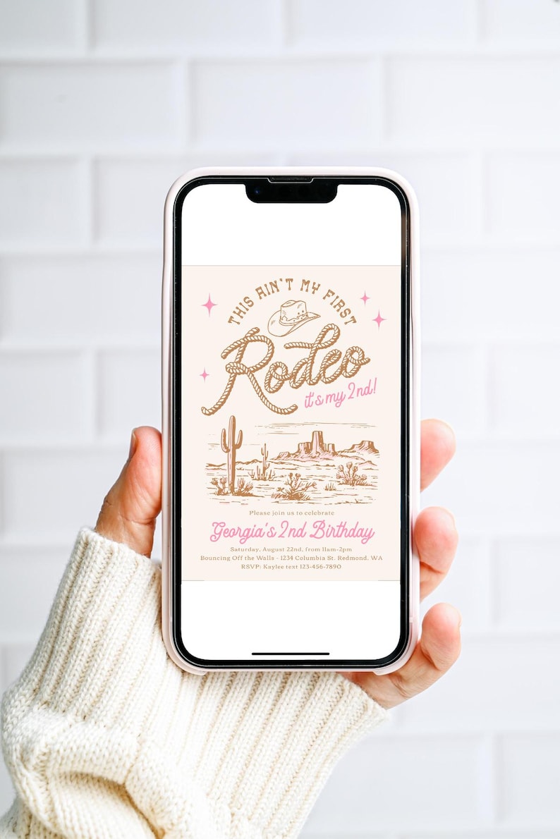 May include: A smartphone displaying a digital invitation with a western theme. The text reads This Ain't My First Rodeo it's my 2nd! Georgia's 2nd Birthday, Saturday, August 22nd, 11am-2pm, Bouncing Off the Walls, 1234 Columbia St. Redmond, WA, RSVP: Kaylee 123-456-7890.
