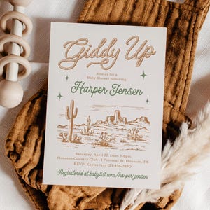 May include: A baby shower invitation with a western theme. The invitation features a drawing of a desert landscape with cacti and mountains. The text on the invitation reads "Giddy Up" and "Join us for a Baby Shower honouring Harper Jensen".