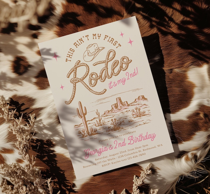 May include: A rectangular invitation card with a cream background featuring the text "THIS AIN'T MY FIRST Rodeo it's my 2nd!" in brown and pink. Below is a desert illustration with cacti and mesas, followed by "Georgia's 2nd Birthday" and event details.