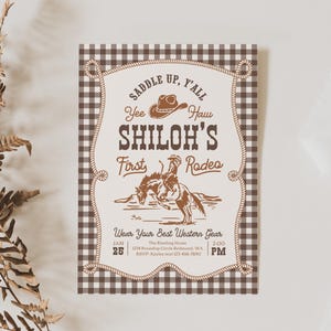 Op de afbeelding: Een rechthoekige uitnodigingskaart met een bruin-witte vichy-ruitrand. Het midden toont een touwframe met de tekst "Saddle Up, Y'all", "Yee Haw", "Shiloh's First Rodeo" en "Wear Your Best Western Gear" met een cowboy op een paard.