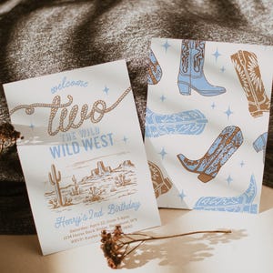 Puede incluir: Una invitación blanca con un diseño de cuerda marrón que dice "welcome two the wild wild west". La invitación es para el 2º cumpleaños de Henry. La invitación tiene un diseño de paisaje del oeste con un cactus y montañas. La invitación también tiene un patrón de botas de vaquero azules y marrones.