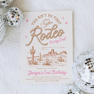 May include: A rectangular birthday invitation card featuring a western theme with a brown rope-style font reading This Ain't My First Rodeo, it's my 2nd, a cowboy hat icon, and a desert landscape illustration with cacti in brown ink on a white background.