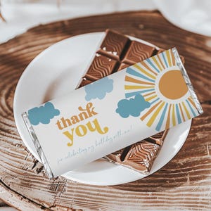 May include: A white chocolate bar wrapper with a sun and clouds design. The wrapper says "thank you" in a retro font and "for celebrating my birthday with me!" in a smaller font.