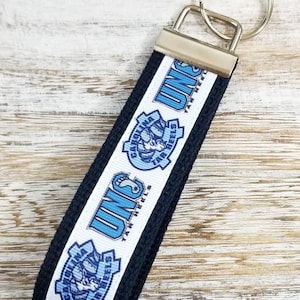 May include: A black and white key chain with a blue and white UNC Tar Heels logo. The keychain has a silver key ring.