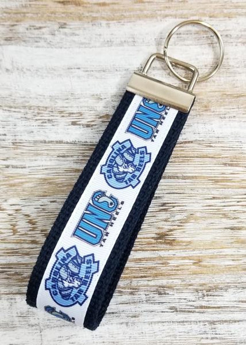 May include: A black and white key chain with a blue and white UNC Tar Heels logo. The keychain has a silver key ring.