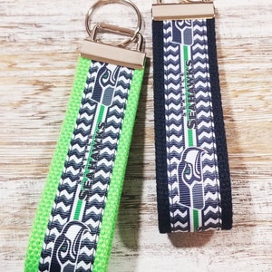 May include: Two keychains with a black and white chevron pattern and a green and white chevron pattern. Both keychains feature a Seattle Seahawks logo and the text "Seattle Seahawks".