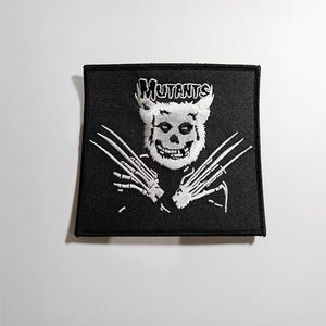May include: White embroidered patch on a black background featuring a skull with claws and the word "Mutants".