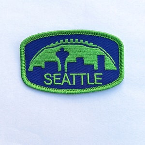 May include: Green and blue embroidered patch with the word "SEATTLE" and a skyline silhouette of the city.