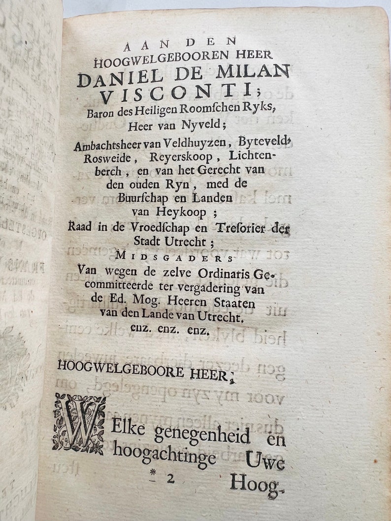 May include: A black and white image of a historical document with text in Dutch. The text reads "Aan den Hoogwelgeboorn Heer Daniel de Milan Visconti; Baron des Heiligen Roomfchen Ryks, Heer van Nyveld; Ambachtsheer van Veldhuyzen, Byteveld> Rosweide, Reyerskoop, Lichten-berch, en van het Gerecht van den ouden Ryn, med de Buurfchap en Landen van Heykoop; Raad in de Vroedſchap en Treforier der Stadt Utrecht; MIDSGADERS Van wegen de zelve Ordinaris Ge-committeerde ter vergadering van de Ed. Mog. Heeren Staaten van den Lande van Utrecht. cuz. enz. enz. HOOGWELGEBOORE HEER; Elke genegenheid en hoogachtinge Uwe Hoog- * 2"