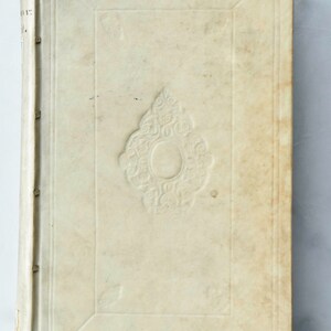 May include: A vintage book with a white leather cover and a decorative embossed design. The book has a spine with raised bands and is in good condition.