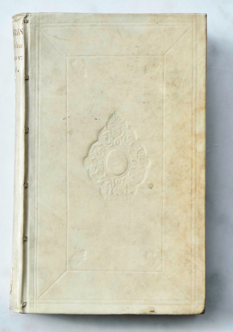 May include: A vintage book with a white leather cover and a decorative embossed design. The book has a spine with raised bands and is in good condition.