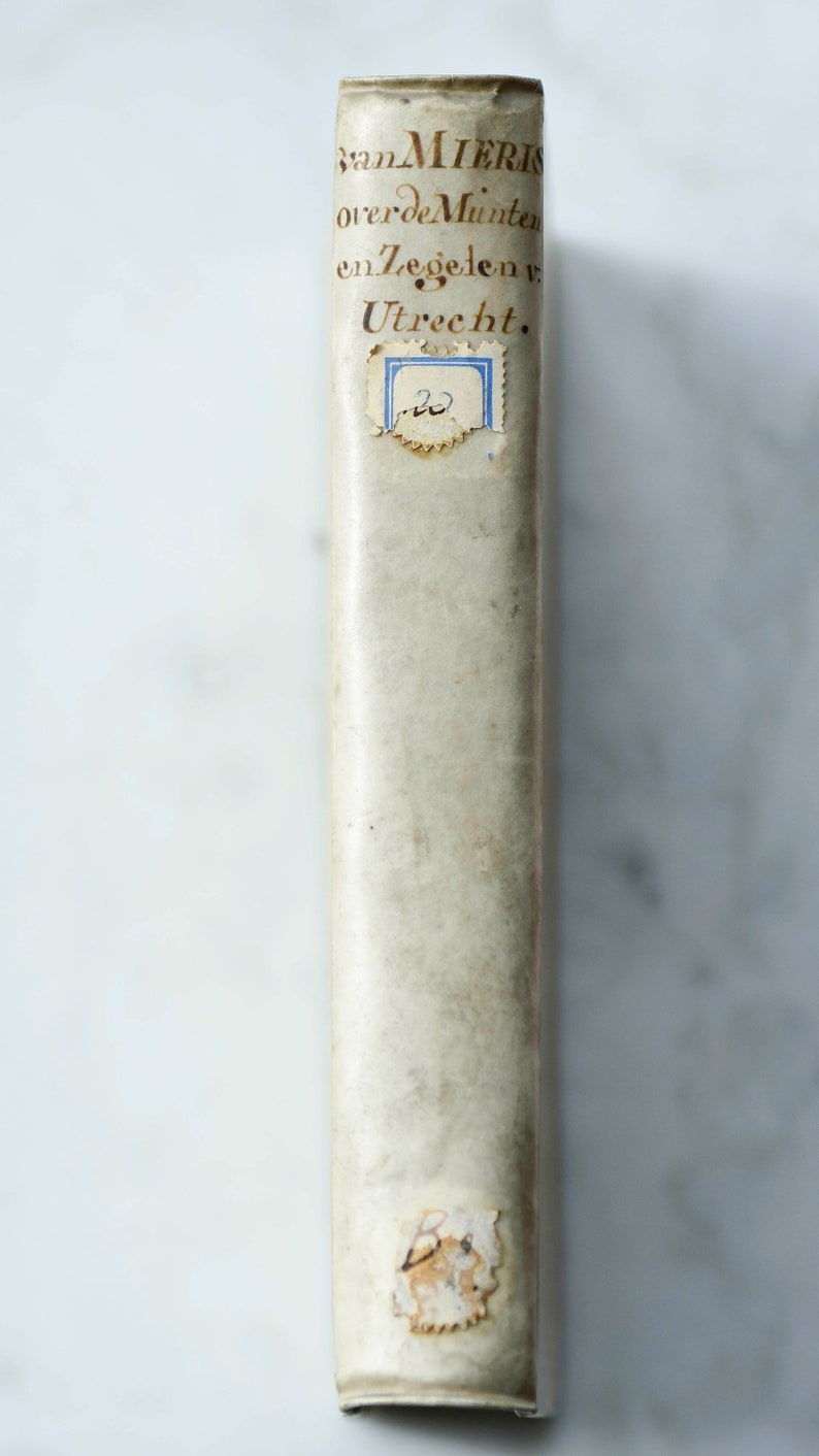 May include: A vintage book with a white cover and brown text that reads "van MIERIS over de Munten en Zegelen v. Utrecht."