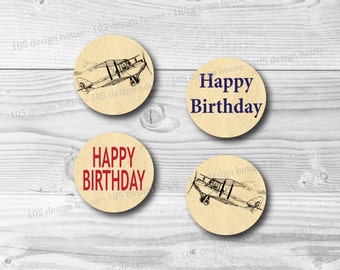 May include: Four round stickers with a vintage airplane illustration and the words "Happy Birthday" in red and navy blue. The stickers have a tan background and are arranged on a light wood surface.
