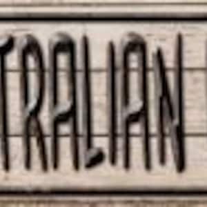 May include: A wooden sign with the text "AUSTRALIAN KELPIE TRAIL" in black lettering. A black and silver silhouette of an Australian Kelpie dog is on the left side of the sign.