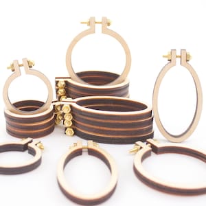 May include: A selection of wooden embroidery hoops in different sizes and shapes. The hoops are made of light-coloured wood with a dark brown inner ring and brass hardware for tightening. The assortment includes round and oval hoops.