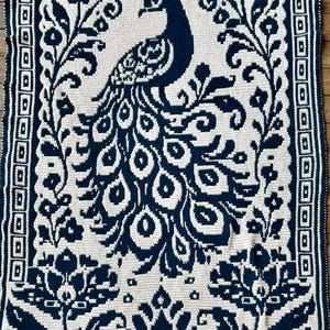 May include: A rectangular crochet blanket featuring a dark navy blue and cream white colour scheme. The design displays a central peacock with an elaborate tail, surrounded by floral motifs and a geometric border pattern along the edges.