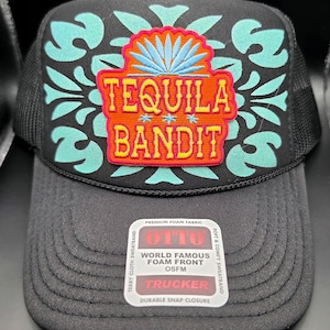 May include: Black trucker hat with a mesh back and a foam front. The front features a colorful design with the words "TEQUILA BANDIT" in orange and teal. The hat includes a "OTTO" label.