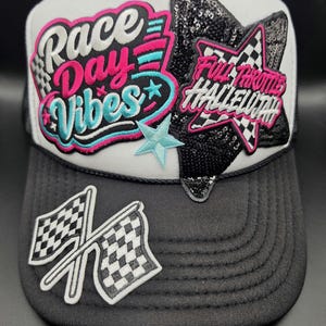 May include: A white and black trucker hat featuring embroidered patches. The front displays the text Race Day Vibes in pink and blue, a black sequined star with the text Full Throttle Hallelujah, and a pair of crossed checkered racing flags.
