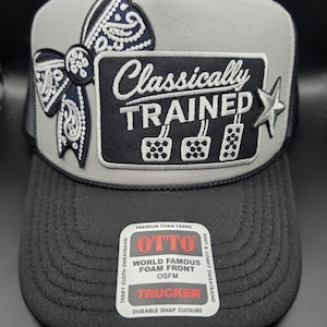 May include: A grey and black trucker hat featuring a dark blue paisley bow patch and a rectangular black patch with the white text Classically Trained above three pedal icons. A silver star is on the right, and an Otto brand sticker is on the brim.