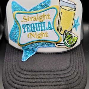 May include: A trucker hat with a white front panel featuring the text "Straight Tequila Night" in a star-shaped design with blue sequins. The design includes a tequila shot and lime slice. The hat has a black brim and mesh back.