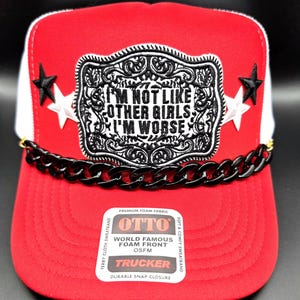 May include: A red and white trucker hat featuring a black and white embroidered patch with the text I'M NOT LIKE OTHER GIRLS I'M WORSE. The hat includes black star accents, a black plastic chain across the brim, and an OTTO brand sticker.
