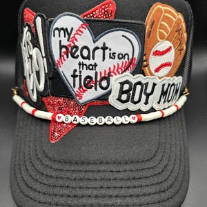 May include: Black baseball cap with a mesh back and a curved brim. The cap features patches with baseball-themed designs, including a heart with the text "my heart is on that field" and the words "BOY MOM". A beaded band spells out "BASEBALL".