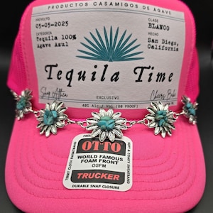 May include: Pink trucker hat with a white label that reads "PRODUCTOS CASAMIGOS DE AGAVE" and "Tequila Time". The hat has a silver chain with turquoise flower charms.