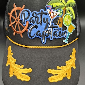 May include: Black trucker hat with the words "Party Captain" in blue and white, along with embroidered images of a ship's wheel, palm tree, and cocktails. The hat has a yellow trim and decorative gold leaf designs.