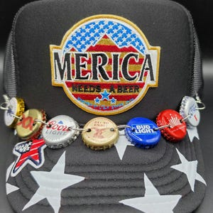 May include: Black trucker hat with a white star pattern on the brim. The hat features a patch with the text "MERICA NEEDS A BEER" and a chain of beer bottle caps.