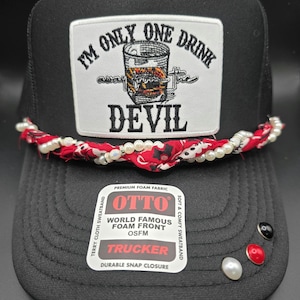 May include: Black trucker hat with a white patch featuring a whiskey glass and the text "I'M ONLY ONE DRINK DEVIL." The hat has a red and white patterned band with pearls, and decorative pins on the brim.