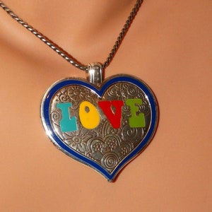 May include: A silver heart-shaped pendant necklace with a blue border and a detailed design. The pendant features the word "LOVE" in colorful enamel letters.