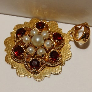May include: A gold pendant with a red and white flower design. The pendant has a detailed design with a scalloped edge.