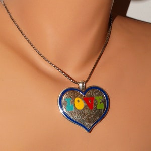 May include: A silver heart-shaped pendant necklace with a blue border and the word "LOVE" spelled out in colorful enamel letters. The pendant has a detailed, swirling pattern.