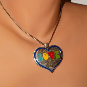 May include: A silver chain necklace with a heart-shaped pendant. The pendant is blue with a silver filigree design and the word "LOVE" spelled out in colorful enamel.