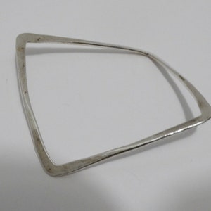May include: A silver bangle bracelet with a simple, geometric design. The bracelet is open and has a slightly curved shape.