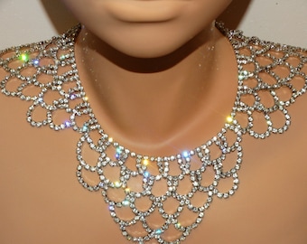 May include: A silver rhinestone choker necklace with a scalloped design. The necklace is made of small, clear rhinestones that are set in a silver metal frame.