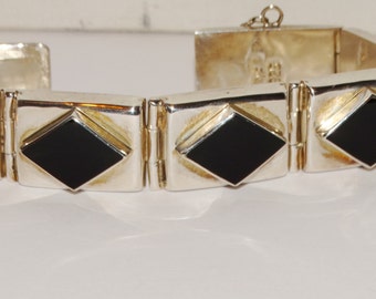 May include: A silver bracelet with black onyx stones set in a diamond shape. The bracelet has a hinged clasp.