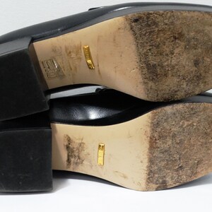 May include: Black leather loafers with a gold logo on the sole. The shoes have a chunky heel and a square toe.
