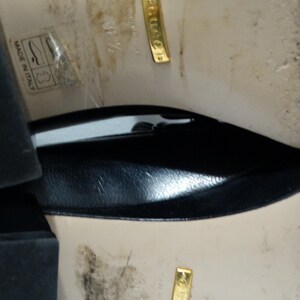 May include: Close-up of the bottom of a pair of black leather shoes. The shoes have a gold label that reads "Gucci" and "Made in Italy".
