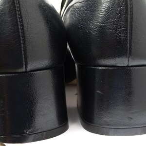 May include: A pair of black leather heeled shoes with a block heel. The shoes have a pointed toe and a smooth leather upper.