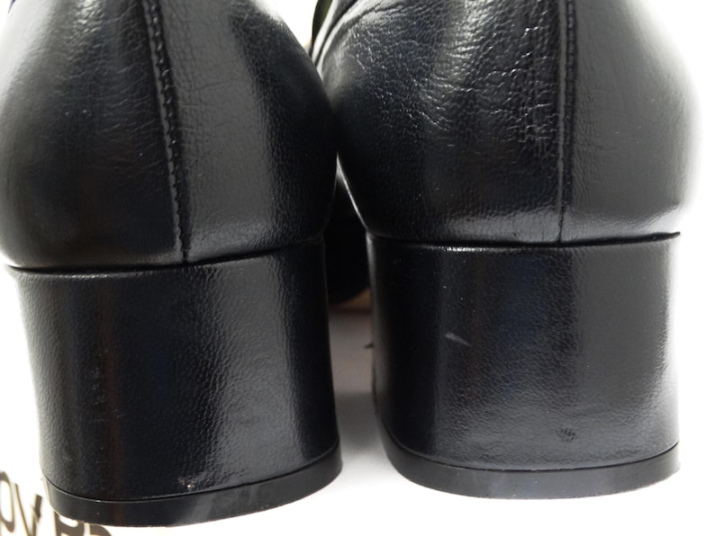 May include: A pair of black leather heeled shoes with a block heel. The shoes have a pointed toe and a smooth leather upper.