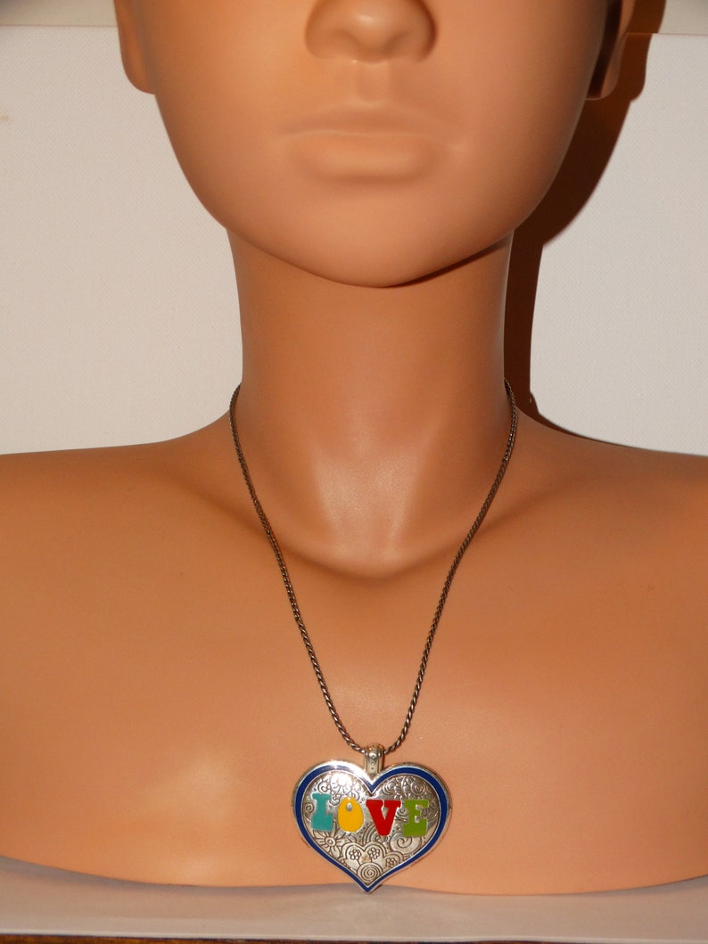 May include: A silver necklace with a heart-shaped pendant. The pendant is decorated with a swirling pattern and the word "LOVE" in colorful enamel.