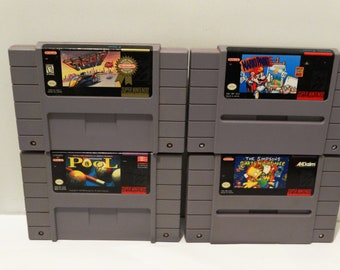 May include: Four Super Nintendo Entertainment System game cartridges. The cartridges are stacked in two pairs. The top row features "Gremlin" and "Mario Paint". The bottom row features "Pool" and "The Simpsons: Bart's Nightmare".