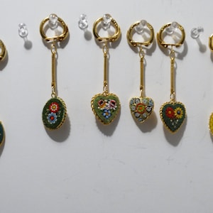 May include: Six keychains with different mosaic designs. Each keychain features a gold-colored metal ring and chain, with a circular or heart-shaped pendant. The pendants are decorated with colorful mosaic tiles depicting floral patterns.